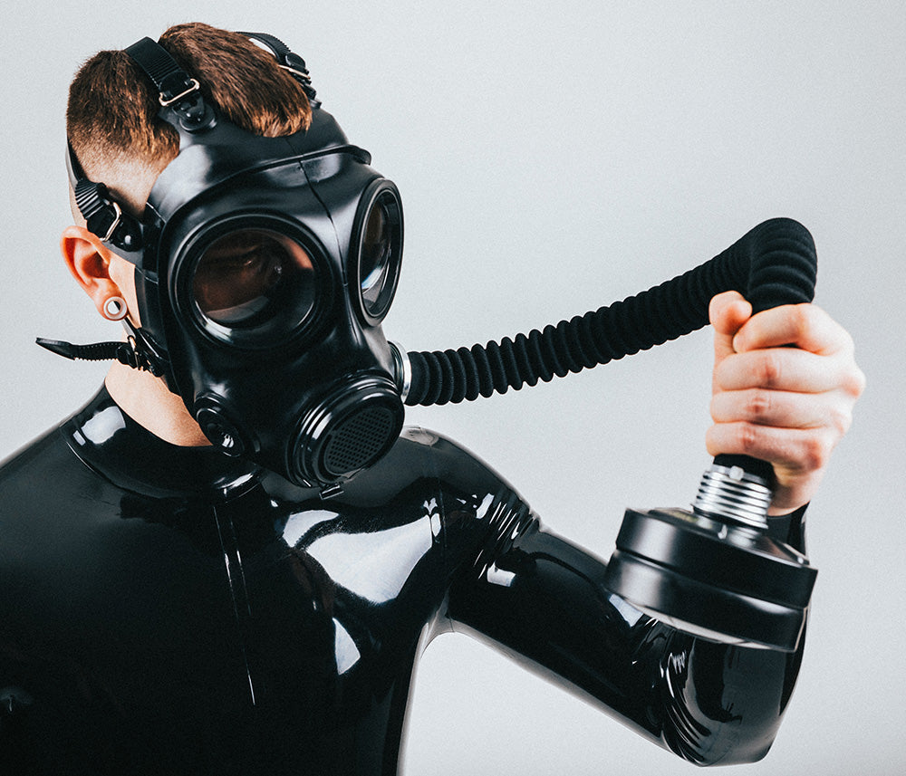 Person wearing a black gas mask with a hose against a gray background